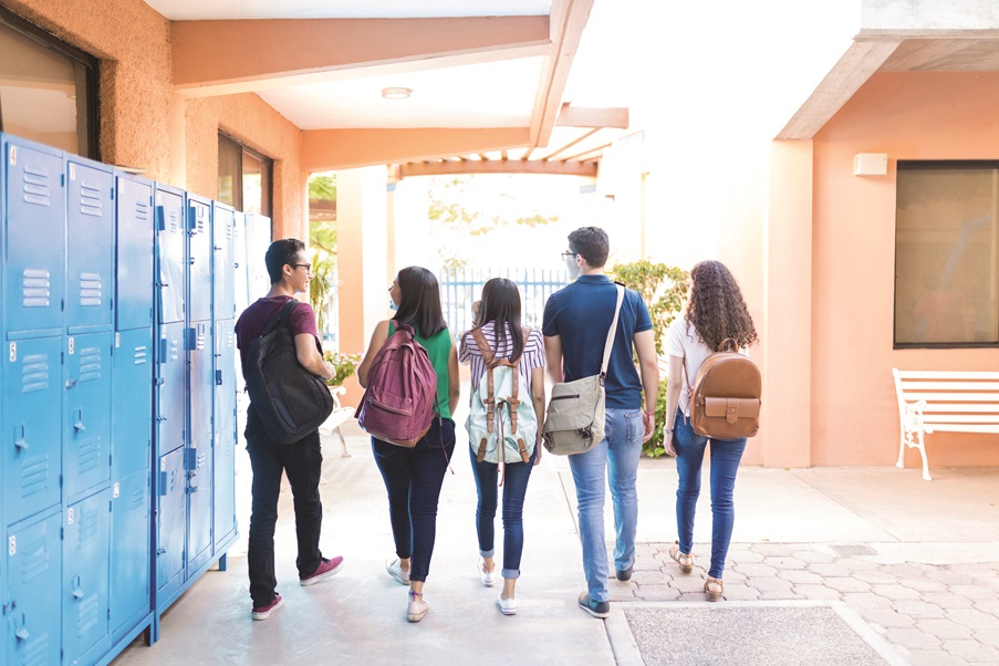 a group of high school students walk down a school corridor lined with lockers. 