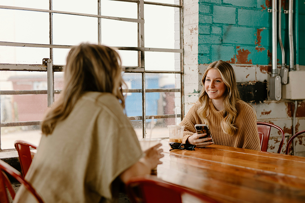 two young women at a grungy coffee shop chatting and smiling glasses and iced coffee on tabletop