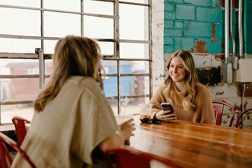 3 - Lessons from the Journey - brooke-cagle-uf1kSx5QsUo-unsplash two young women at a grungy coffee shop chatting and smiling glasses and iced coffee on tabletop