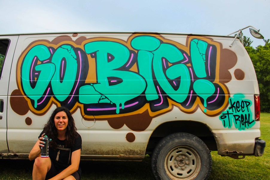 Laura Bronson in front of a van spray painted to read "go big! Keep it real"